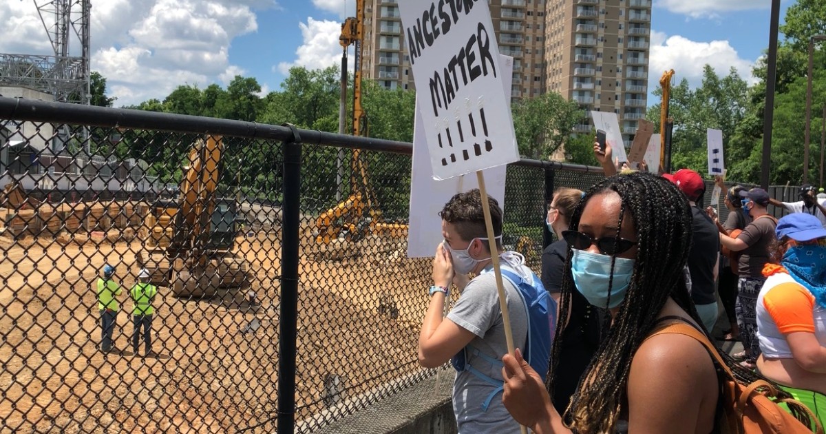 Multiracial group of demonstrators holding signs and protesting outside fenced construction site
