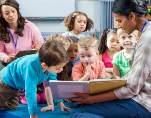 photo of teacher reading picture book to nursery school students