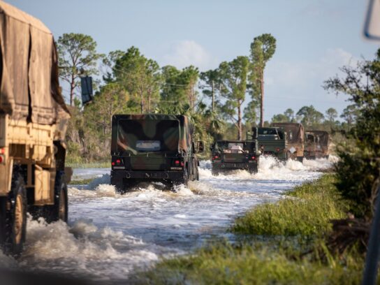 Florida National Guard vehicles mobilizing over a flooded road to provide aid for Hurricane Helene victims.