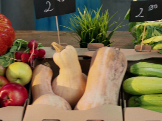 Squash, apples and vegetables in crates at a farm market stand.