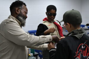 An Alpha Phi Alpha member helps two Scouts in uniform during Alpha Merit Badge University.