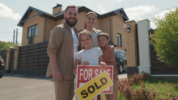 Family standing in front of a new home, posing with "Sign for Sale" and "Sold" sticker on it